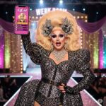 Drag queen holding a phone featuring RuPaul's Drag Race Superstar game on a sparkling runway stage